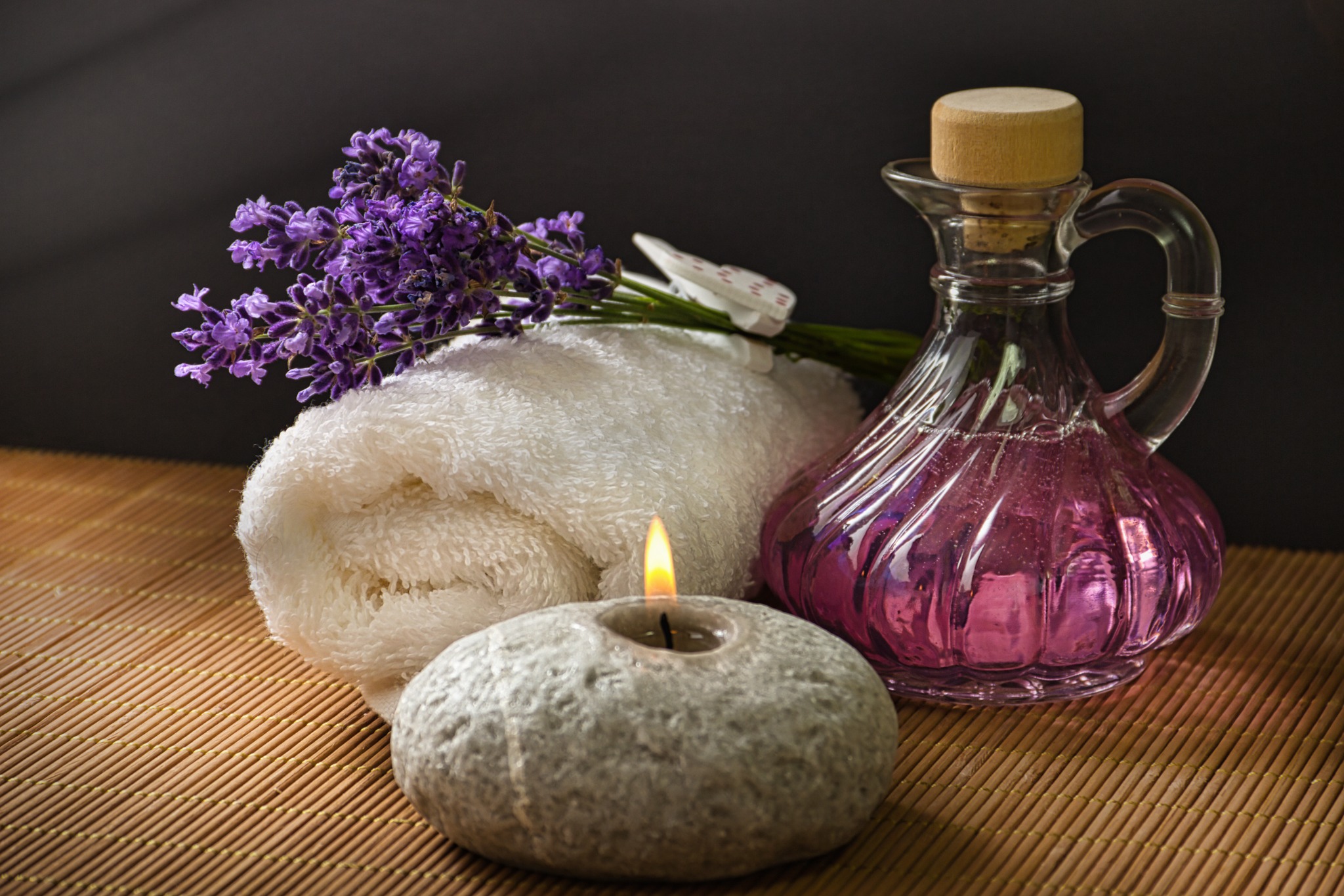 Flores de lavanda junto a un frasco de aceite, una toalla y una vela de spa